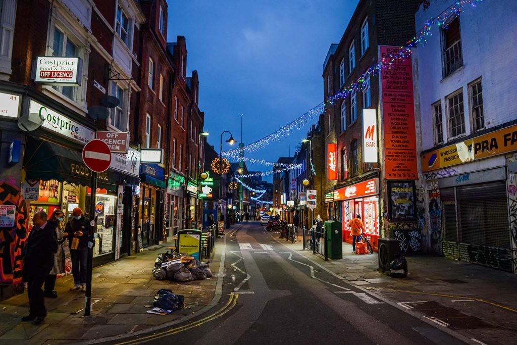 Walking down Brick Lane, East London, in the evening, with shop neon lights and festive lights glowing in the dusk..